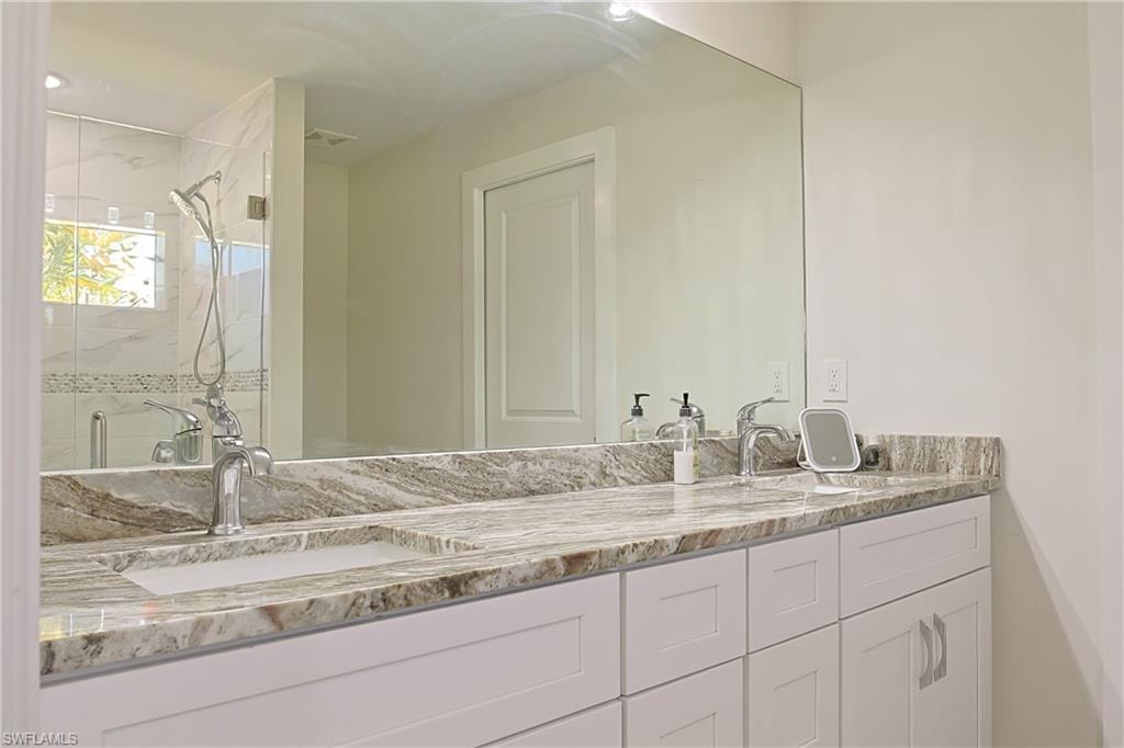 Dual vanity with stone countertop, undermount sinks, chrome faucets, and white shaker-style cabinetry