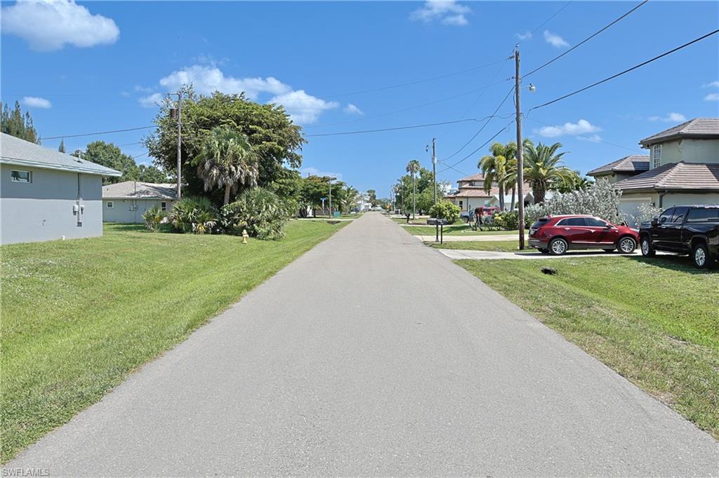Residential street with paved roadway, lush green lawns, and mature tropical landscaping