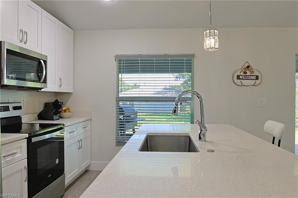 White shaker cabinetry with brushed nickel hardware, stainless steel appliances, a large island with an undermount stainless steel sink, a chrome high-arc faucet, and light-toned countertops