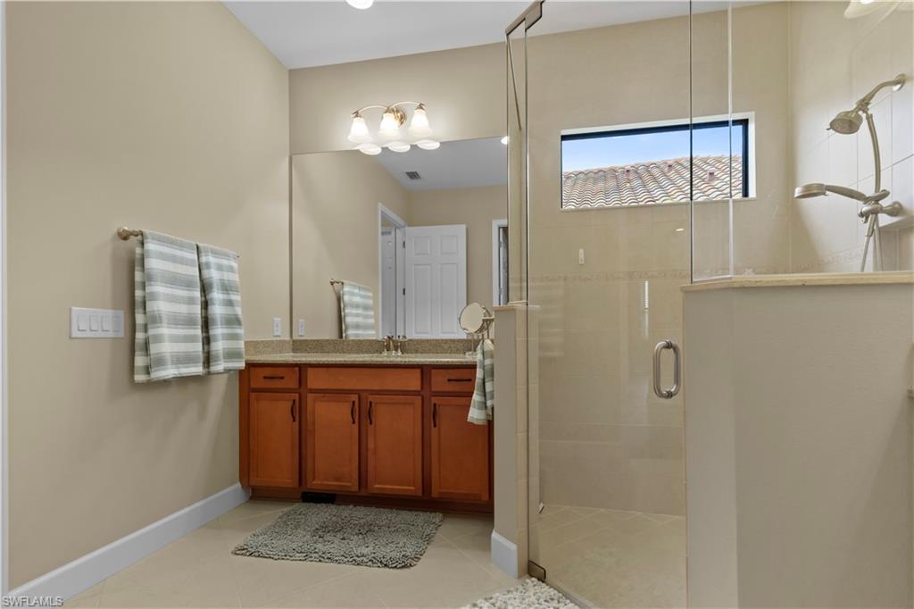 Bathroom featuring a glass-enclosed shower, wood-finish vanity with countertop, large wall-mounted mirror, and tile flooring