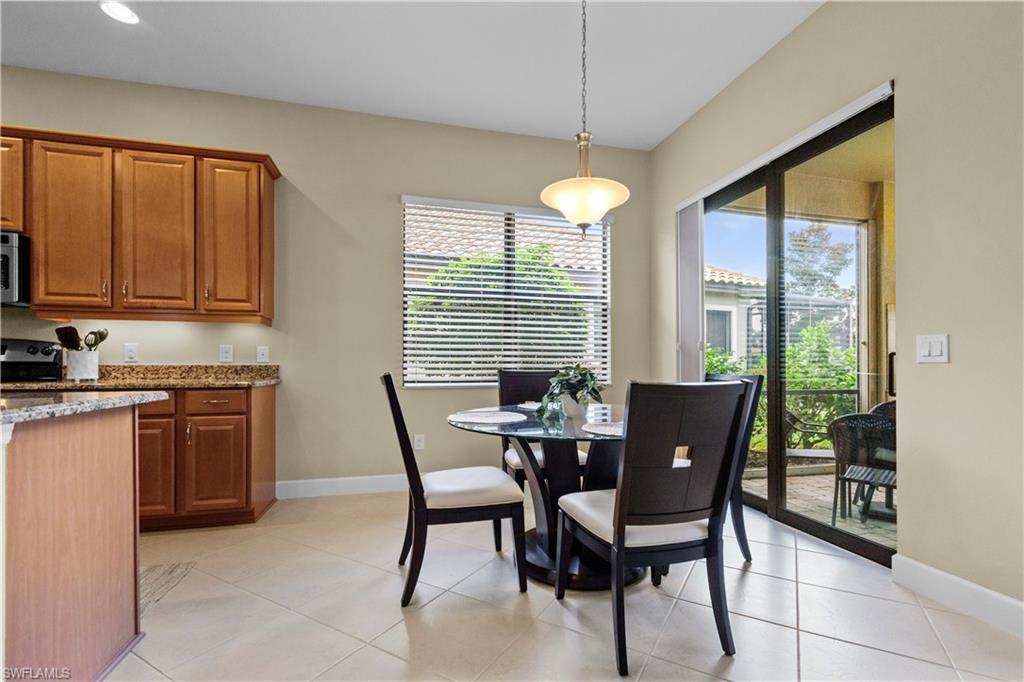 Kitchen and dining area featuring warm-toned cabinetry, granite countertops, tile flooring, and a sliding glass door leading to an outdoor space
