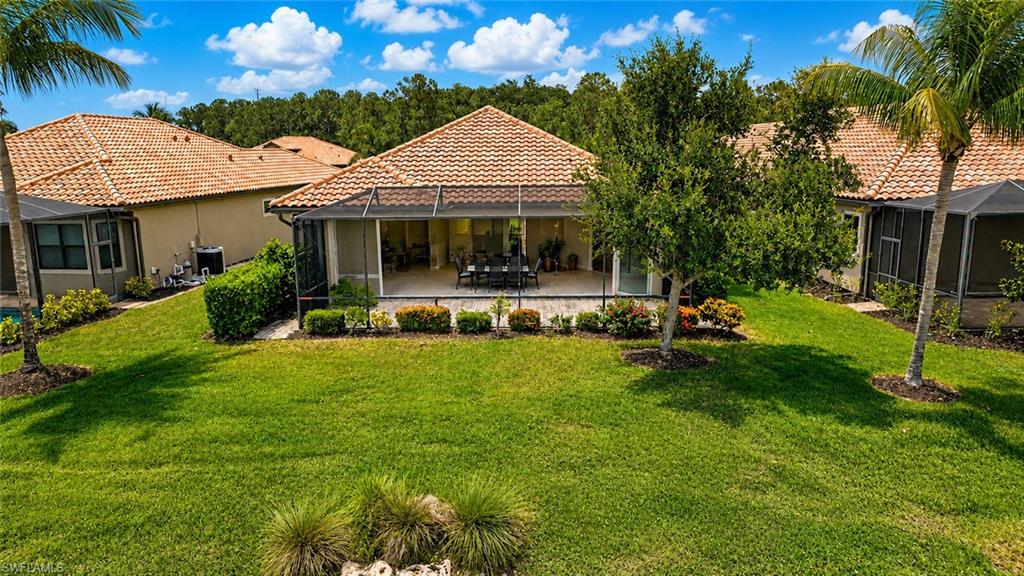 Expansive rear exterior featuring a screened lanai with accordian shutters, tile roofing, stucco siding, and mature landscaping
