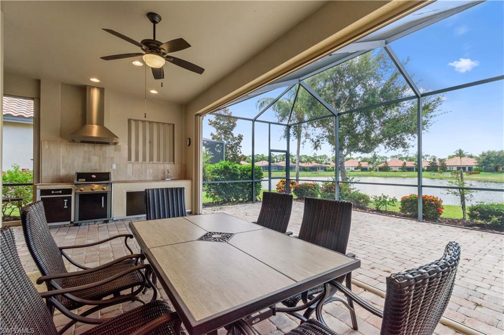 Screened patio featuring a built-in outdoor kitchen with stainless steel appliances, a ceiling fan, and paver flooring