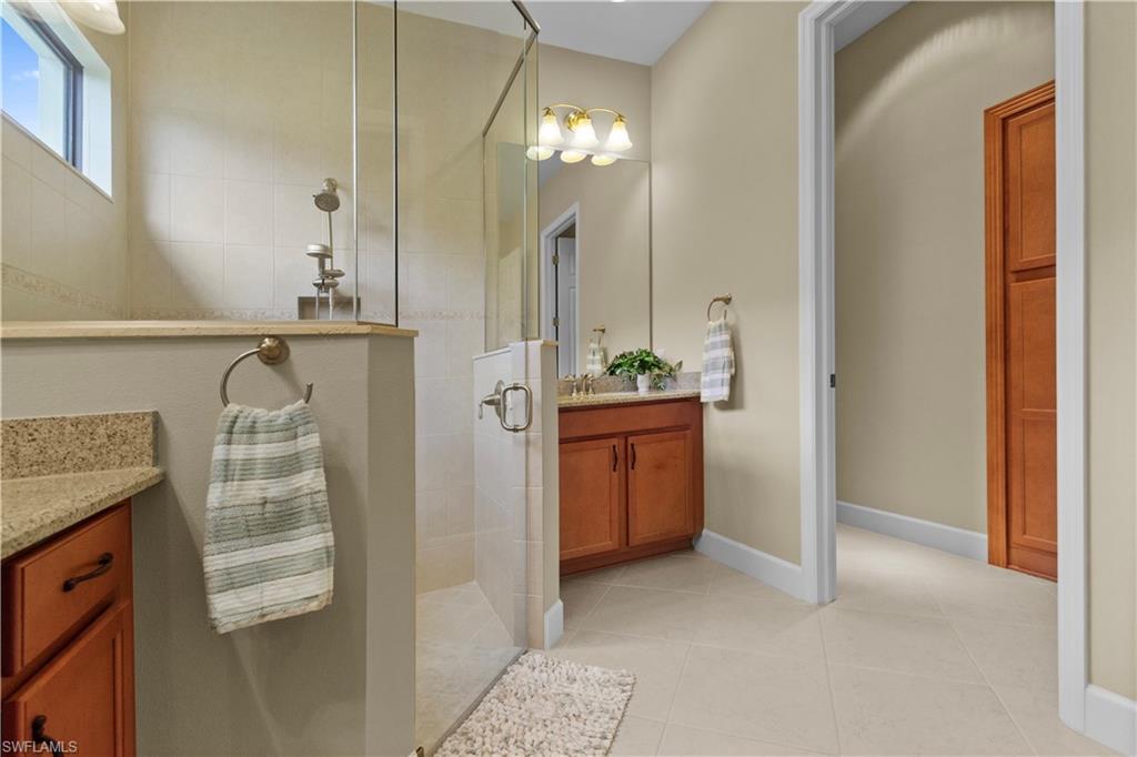 Spacious bathroom featuring a glass-enclosed shower with tiled walls, dual wood-finish vanity cabinets with granite-style countertops, and a full-height wood-finish storage cabinet