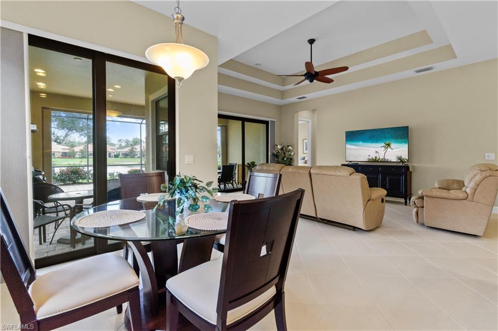 Open-concept dining and living area featuring expansive glass sliding doors, tray ceiling with a ceiling fan, and large format tile flooring