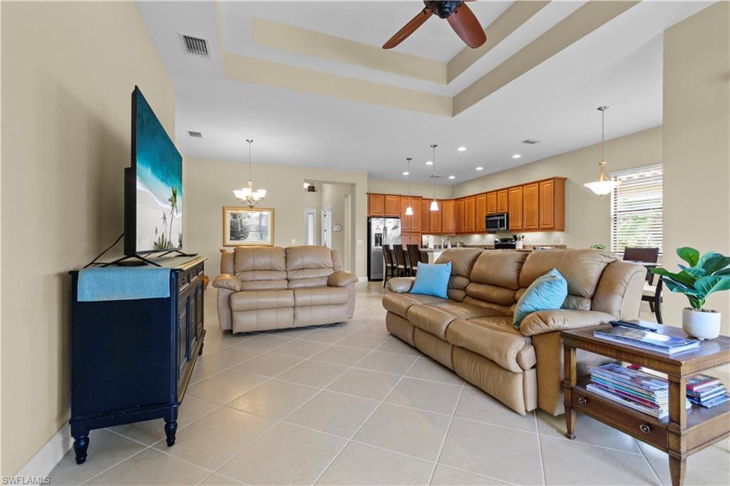 Expansive open-concept living area featuring a tray ceiling with a ceiling fan, recessed lighting, and large format tile flooring