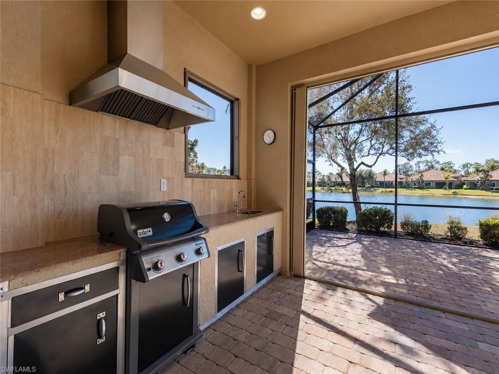 Outdoor kitchen featuring a built-in grill, stainless steel range hood, stone tile backsplash, and integrated cabinetry