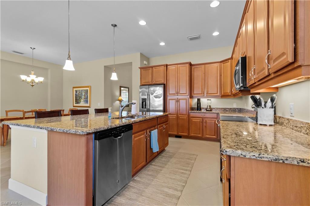 Open-concept kitchen featuring an expansive island with pendant lighting, stone countertops, stainless steel appliances, abundant wood cabinetry, and recessed lighting