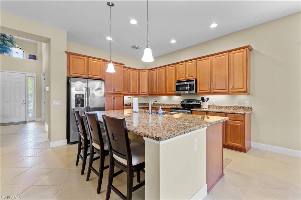 Open-concept kitchen featuring an expansive center island with seating, granite countertops, wood cabinetry, stainless steel appliances, and recessed lighting