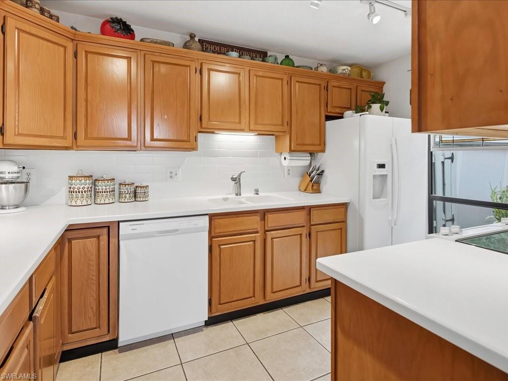 Kitchen featuring light wood cabinetry, white countertops, white subway tile backsplash, a double basin sink with a chrome faucet, and tile flooring
