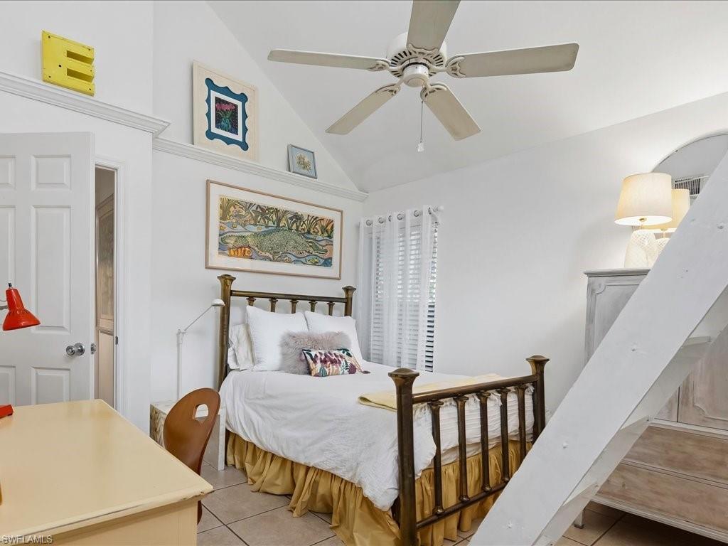 Vaulted ceiling bedroom featuring a ceiling fan, tiled flooring, built-in shelving, and white interior door