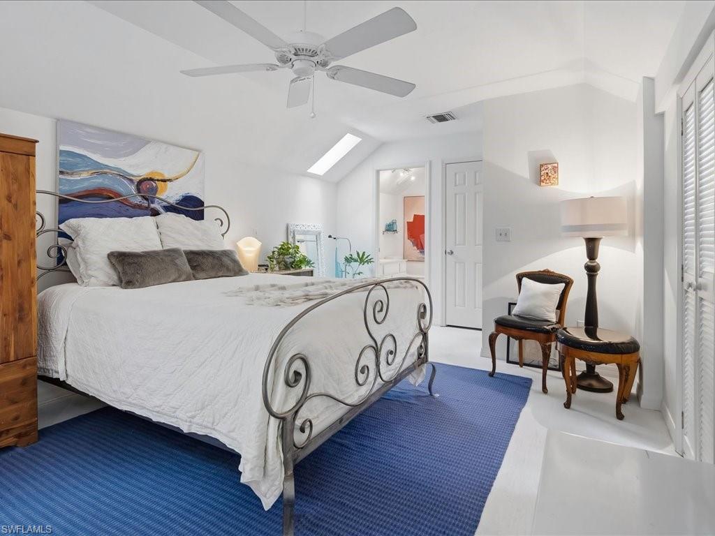 Vaulted ceiling room featuring white-painted wood flooring, a ceiling fan, and a skylight