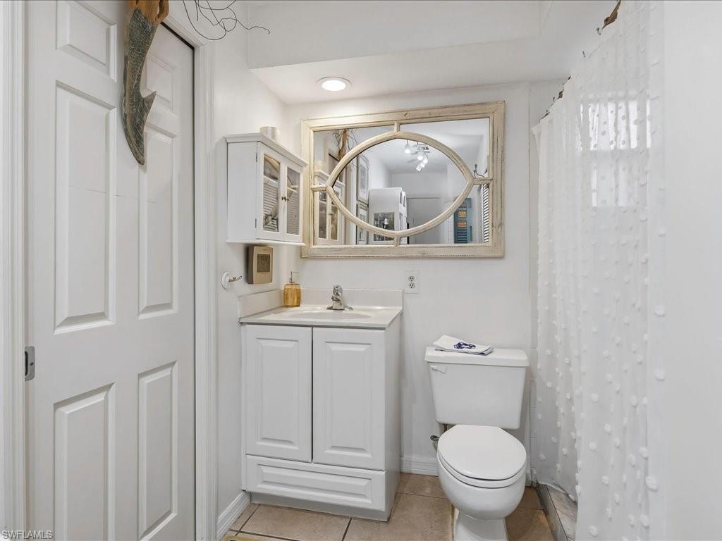 Bathroom featuring a white vanity with integrated sink, a built-in wall cabinet, a toilet, and tiled flooring