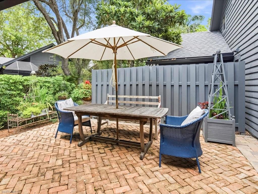 Brick paver patio featuring a gray privacy fence, lush green foliage