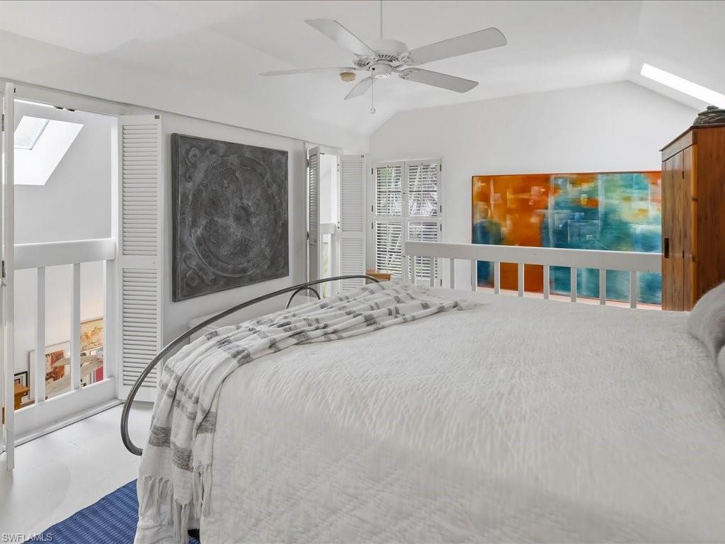 Vaulted ceiling with skylight, featuring a white ceiling fan, white flooring, and a white balustrade overlooking a lower level