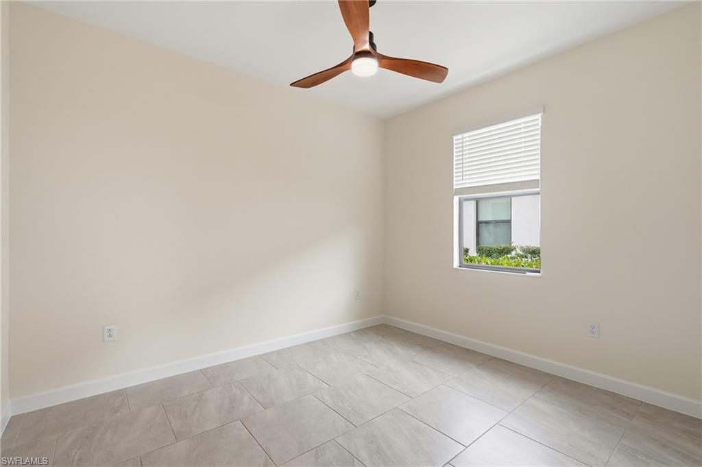 Neutral-toned room featuring a wood-finish ceiling fan with integrated lighting, a window with horizontal blinds, and large format tile flooring