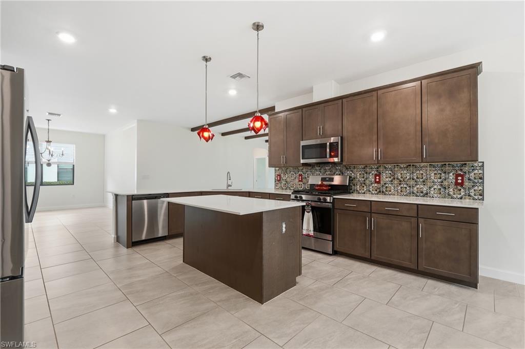 Open-concept kitchen featuring an island with a white countertop, full-height cabinetry with brushed nickel hardware, stainless steel appliances, and a patterned tile backsplash