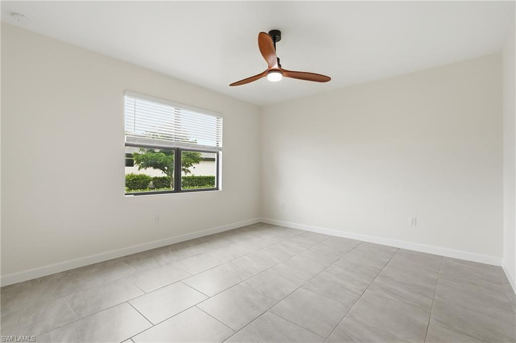 Spacious room featuring light-toned walls, tile flooring, and a modern ceiling fan with wood-finish blades