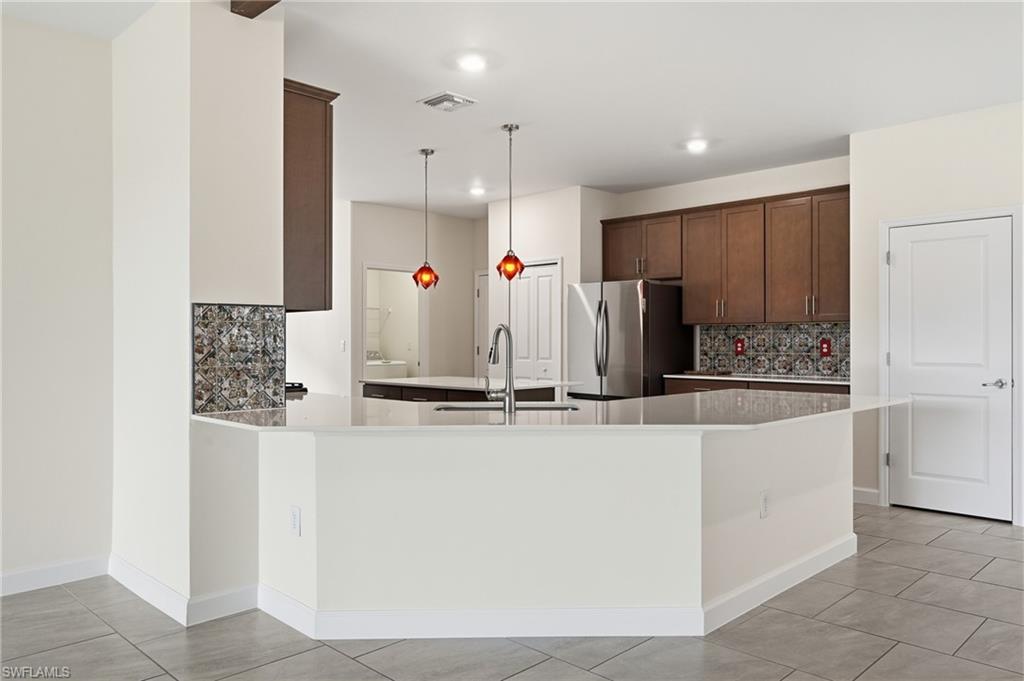 Open-concept kitchen featuring an eat-at counter, stainless steel appliances, dark wood cabinetry, and a decorative tile backsplash