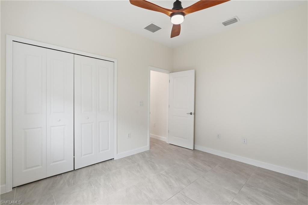 Room featuring light gray tile flooring, crisp white walls, and a wood-finish ceiling fan with integrated lighting