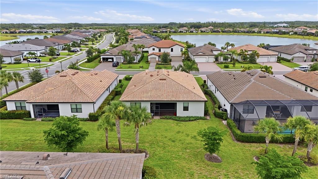 Aerial neighborhood overview featuring a lake, mature landscaping, and uniform tile roofing