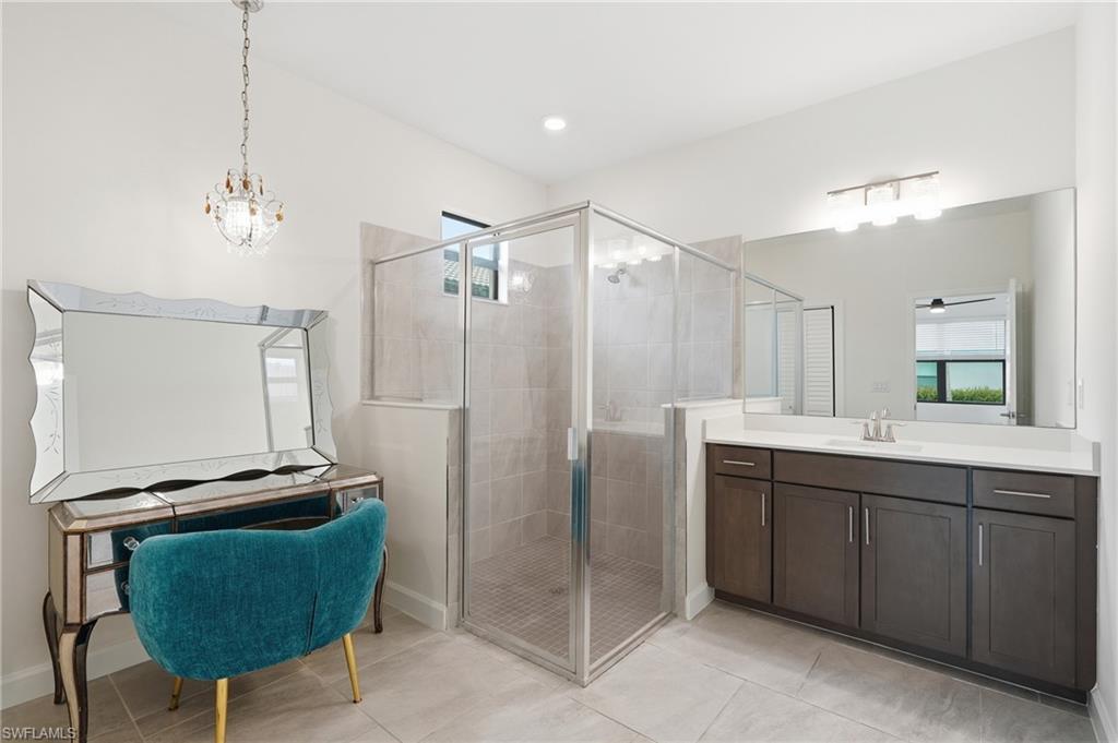 Spacious bathroom featuring a glass-enclosed shower with tile surround, a large vanity with ample storage, a wide mirror, and a contemporary chandelier