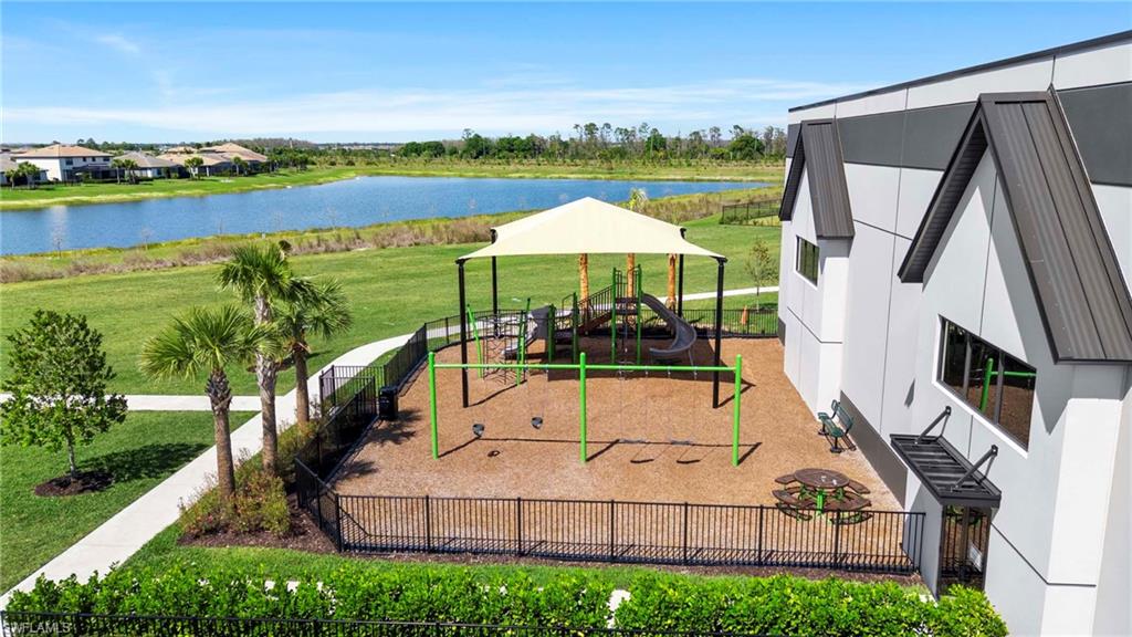Recreational playground with a shade canopy, surrounded by lush green landscaping and bordered by a serene lake