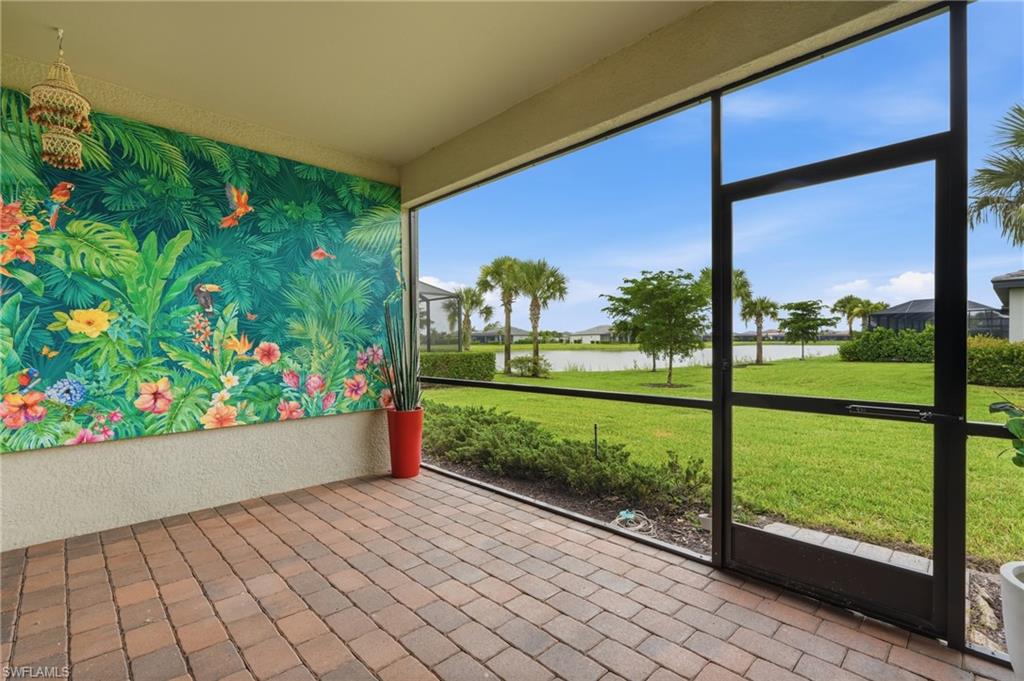 Screened-in patio featuring paver flooring, a vibrant mural wall, and expansive outdoor space with a distant water feature