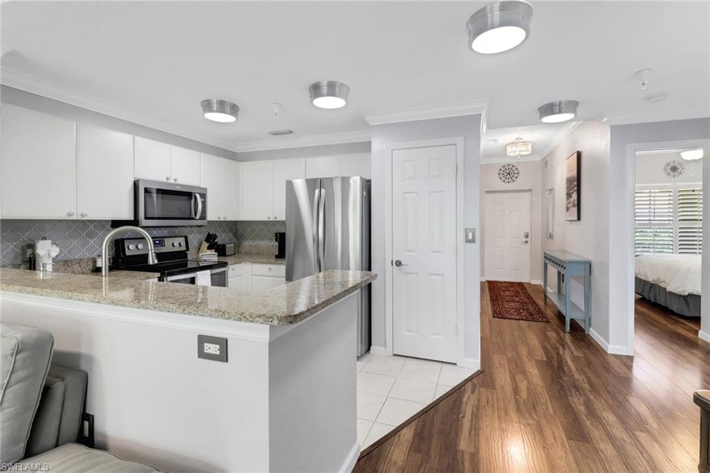 Kitchen featuring appliances with stainless steel finishes, a peninsula, light wood-type flooring, light stone countertops, and crown molding