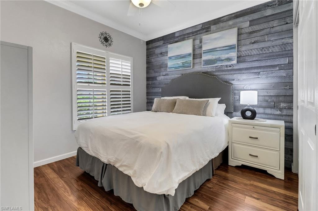 Bedroom with an accent wall, dark wood finished floors, crown molding, baseboards, and ceiling fan