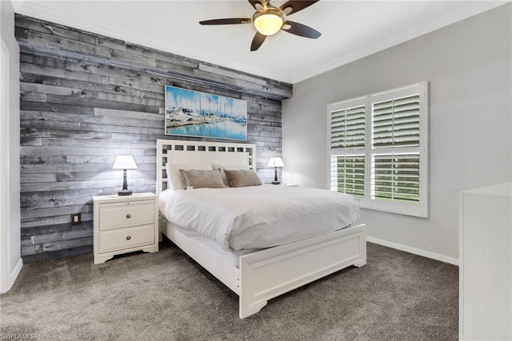 Carpeted bedroom featuring ornamental molding, ceiling fan, baseboards, and wooden walls