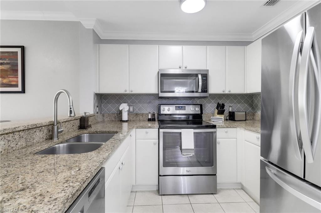 Kitchen featuring appliances with stainless steel finishes, a sink, light tile patterned flooring, ornamental molding, and tasteful backsplash