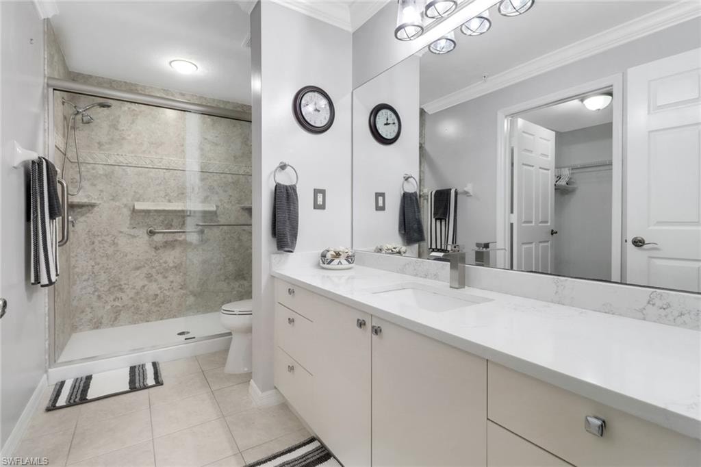 Bathroom with toilet, a stall shower, vanity, crown molding, and baseboards