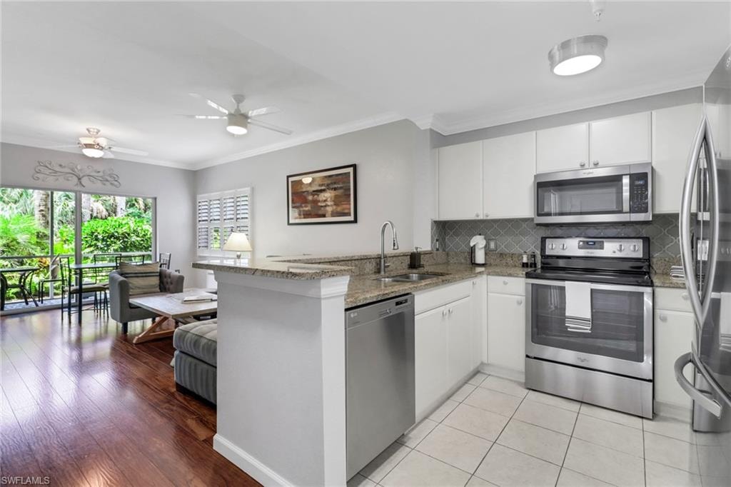Kitchen with appliances with stainless steel finishes, a sink, a peninsula, light stone countertops, and ornamental molding