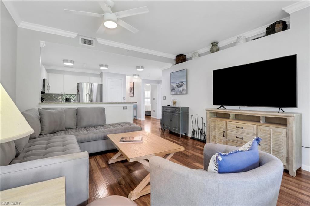 Living room featuring dark wood-type flooring, crown molding, a ceiling fan, and baseboards