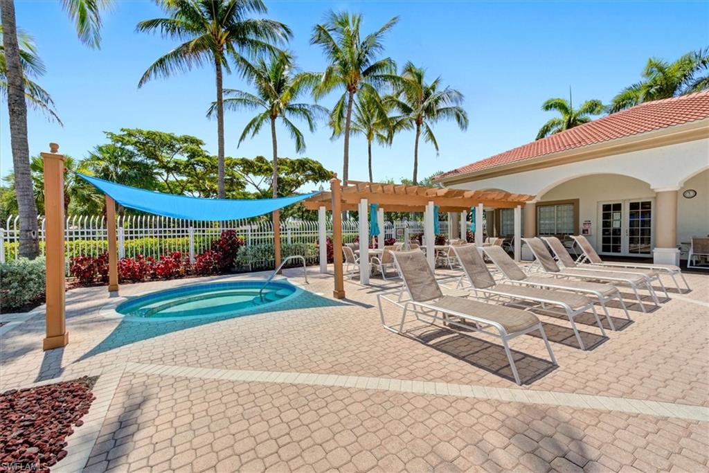 Resort-style outdoor area featuring a tiled spa with a blue shade sail, a pergola-covered dining space, and a paver patio