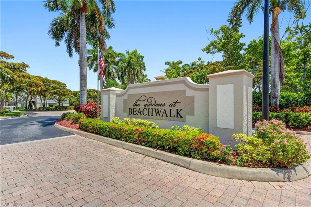 Entry monument featuring "The Gardens at Beachwalk" inscription, flanked by lush landscaping and mature palm trees
