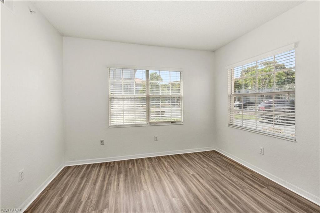 Bright interior space featuring wood-finish flooring, two windows with blinds, white walls, and white trim
