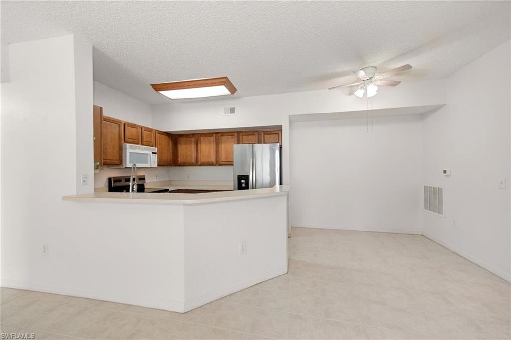 Open-concept kitchen and dining area featuring warm wood cabinetry, stainless steel appliances, a breakfast bar, and tile flooring
