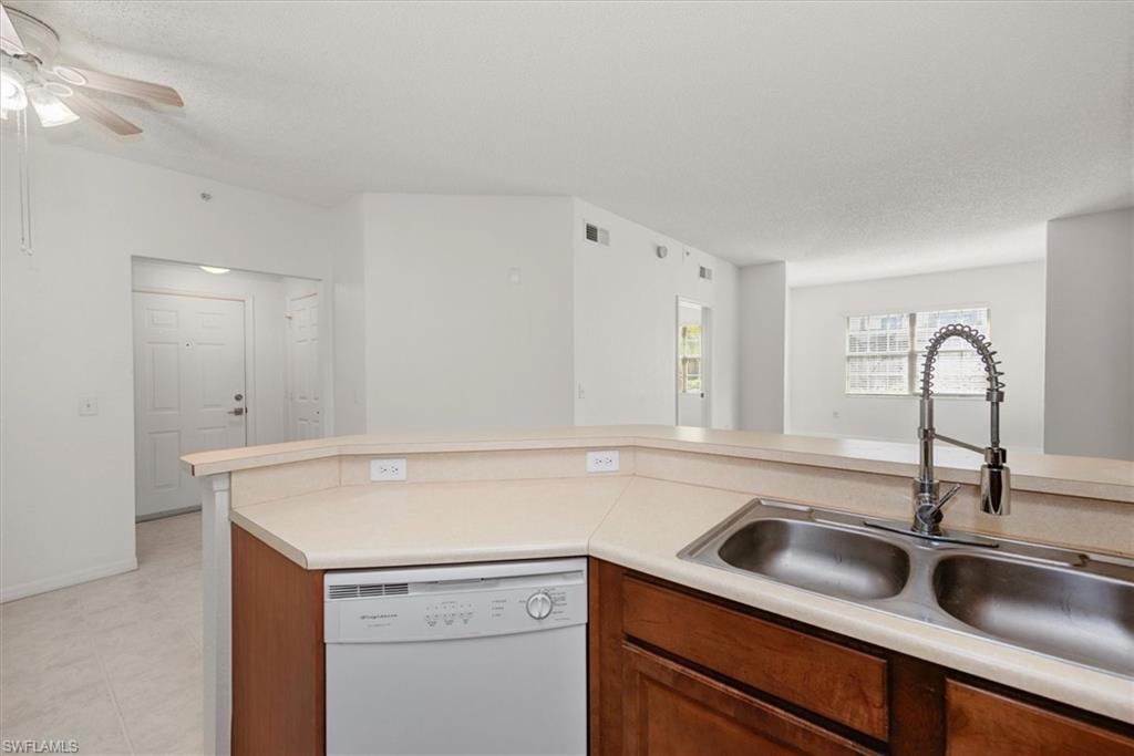 Kitchen island featuring a double basin stainless steel sink with a high-arc faucet, integrated dishwasher, and countertop