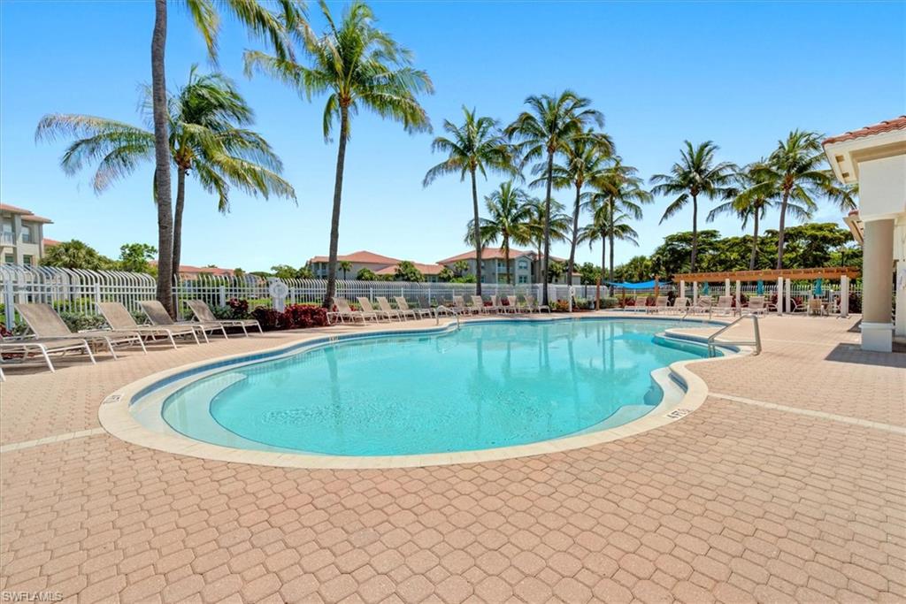 Resort-style pool area featuring a freeform pool, paver deck, palm trees, and a shaded pergola