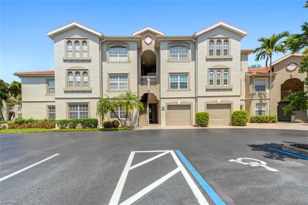 Multi-story stucco exterior featuring a terra cotta tile roof, arched architectural details, integrated single-car garages, and mature tropical landscaping