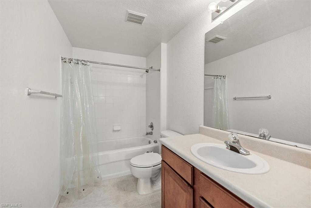 Bathroom featuring a wood-finish vanity with an integrated sink and light-toned countertop, an overhead vanity light, a large mirror, a toilet, and a white tub with tile surround