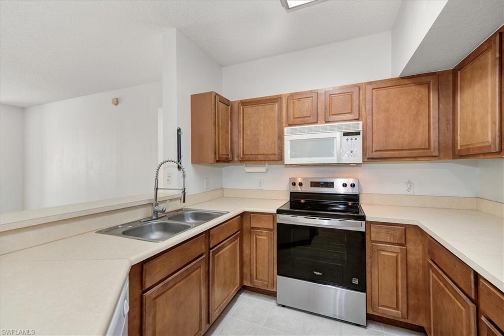 Kitchen featuring wood cabinetry, light countertops, stainless steel appliances, and a double basin sink with a high-arc faucet