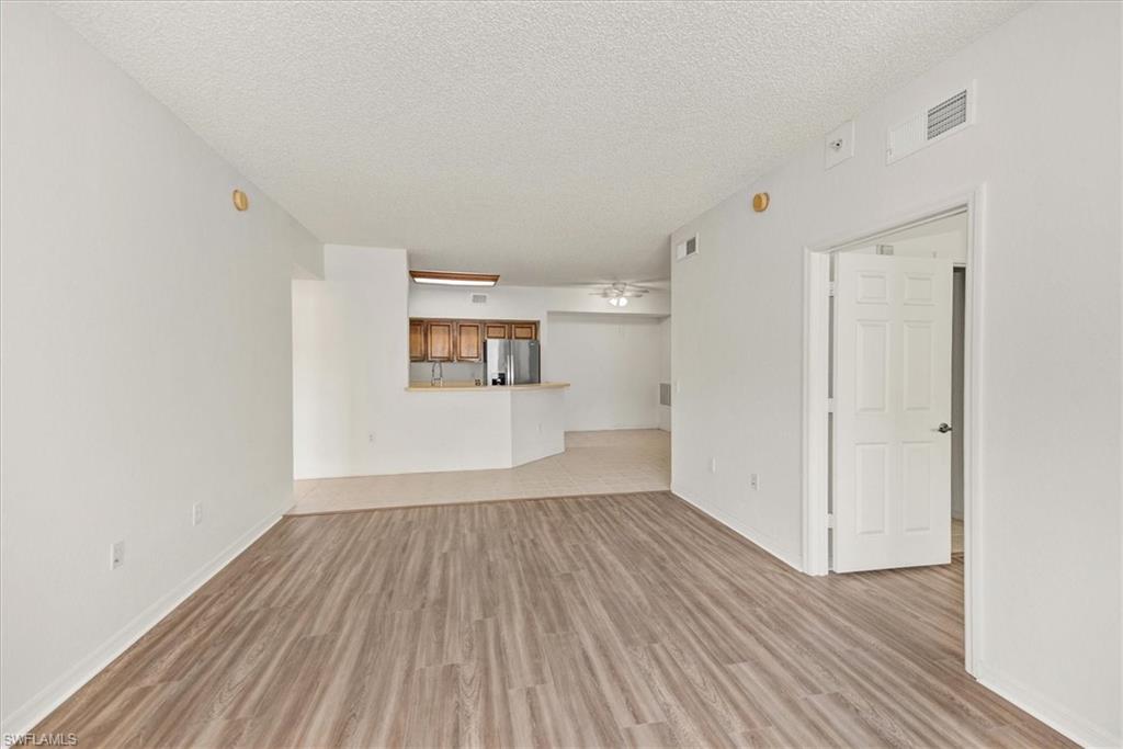 Spacious room with wood-finish flooring, white painted walls, and a textured ceiling