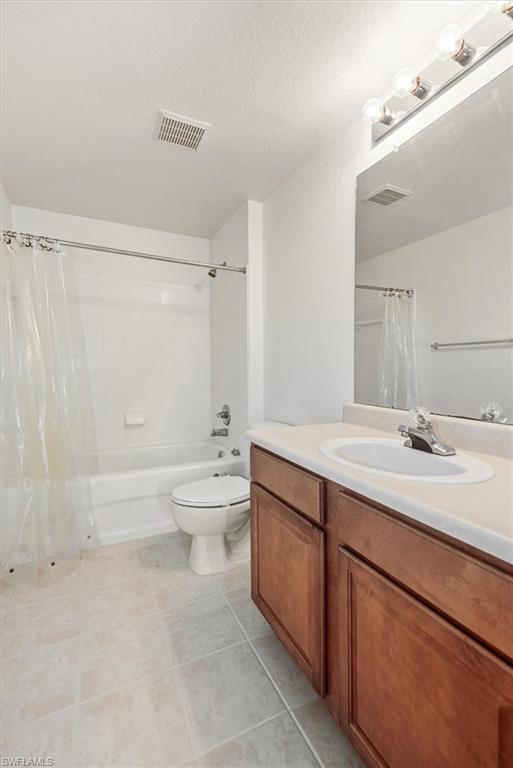 Bathroom featuring a wood-finish vanity with an integrated sink, a white bathtub with a shower, and light-toned tile flooring