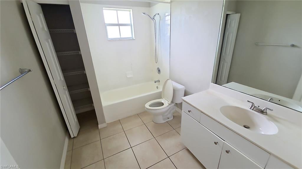 Bathroom featuring a single vanity with an integrated sink, a large wall-mounted mirror, a bathtub with an overhead shower, and neutral floor tiling