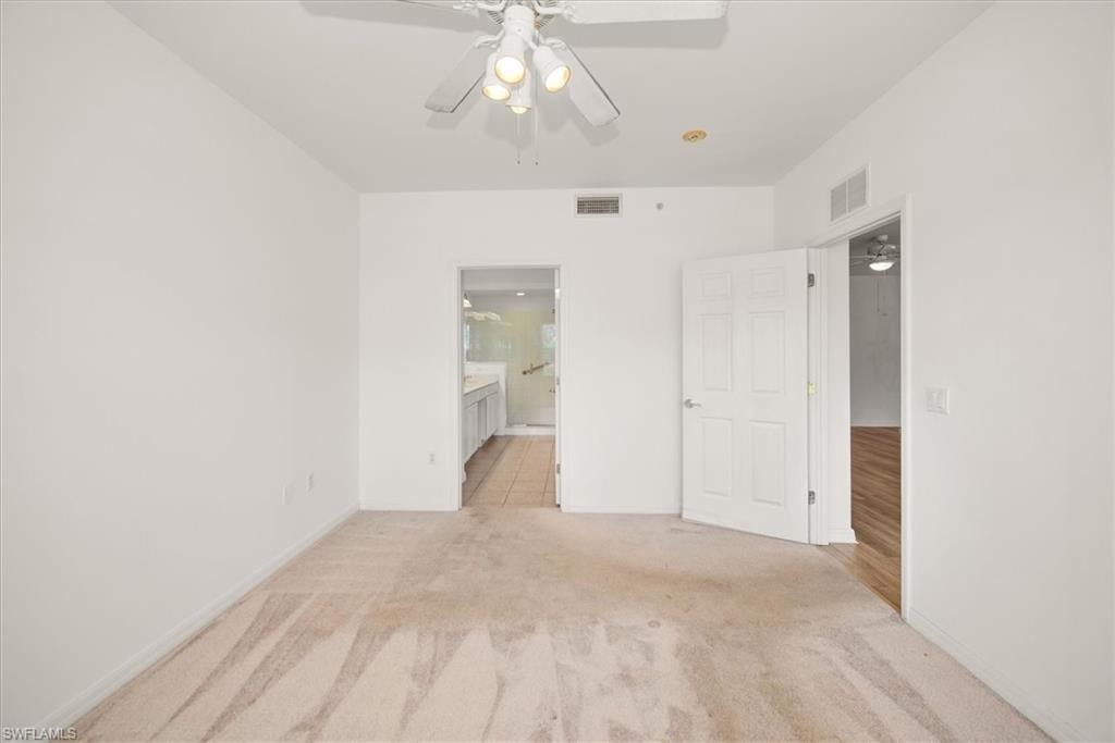 Carpeted room featuring a ceiling fan with integrated lighting, a doorway to a bathroom with tile flooring, and a separate doorway to a room with wood-finish flooring
