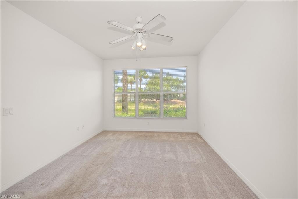 featuring neutral carpet flooring, a large window with horizontal blinds overlooking exterior trees, and a ceiling fan with integrated lighting