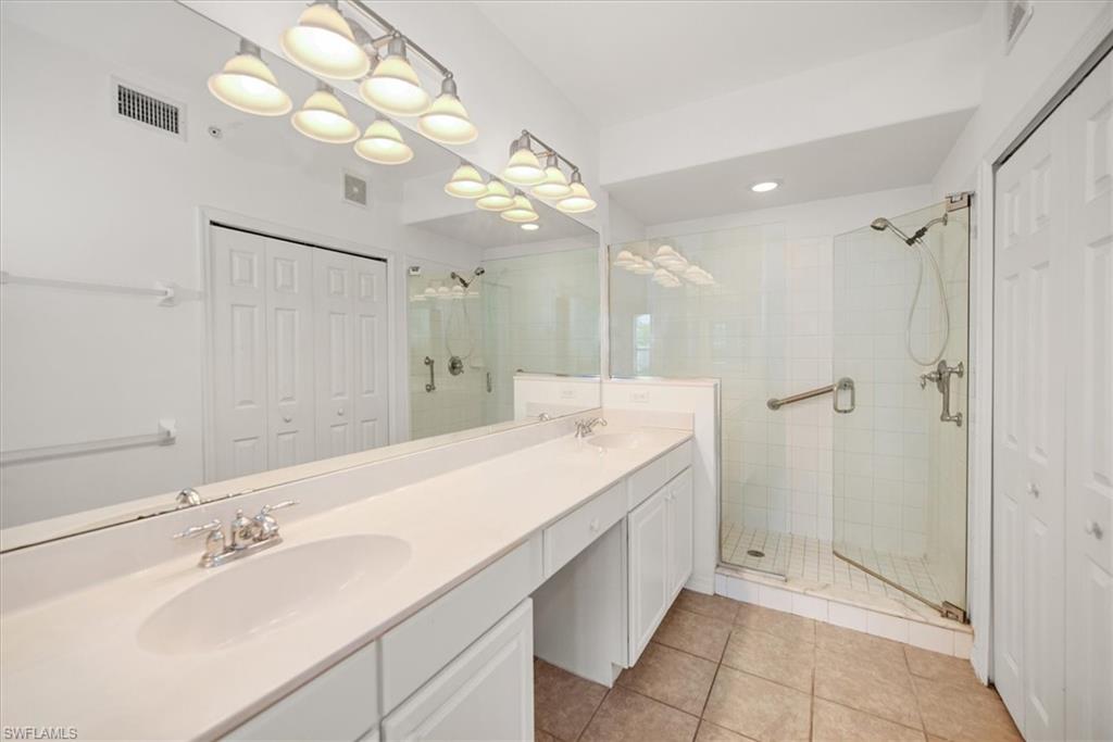 featuring a double vanity with integrated sinks, a glass-enclosed shower with a tiled surround, a large wall-mounted mirror, and tile flooring